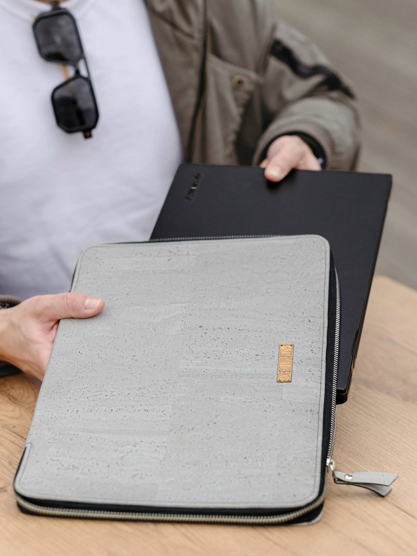 Person holding a gray laptop sleeve and black laptop on a wooden surface