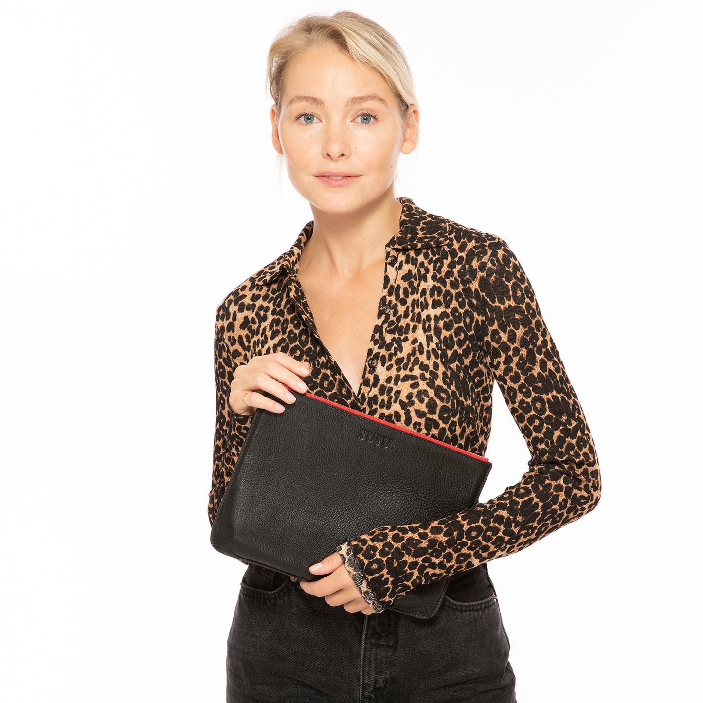 Woman wearing a leopard print shirt holding a black clutch bag with a red interior.