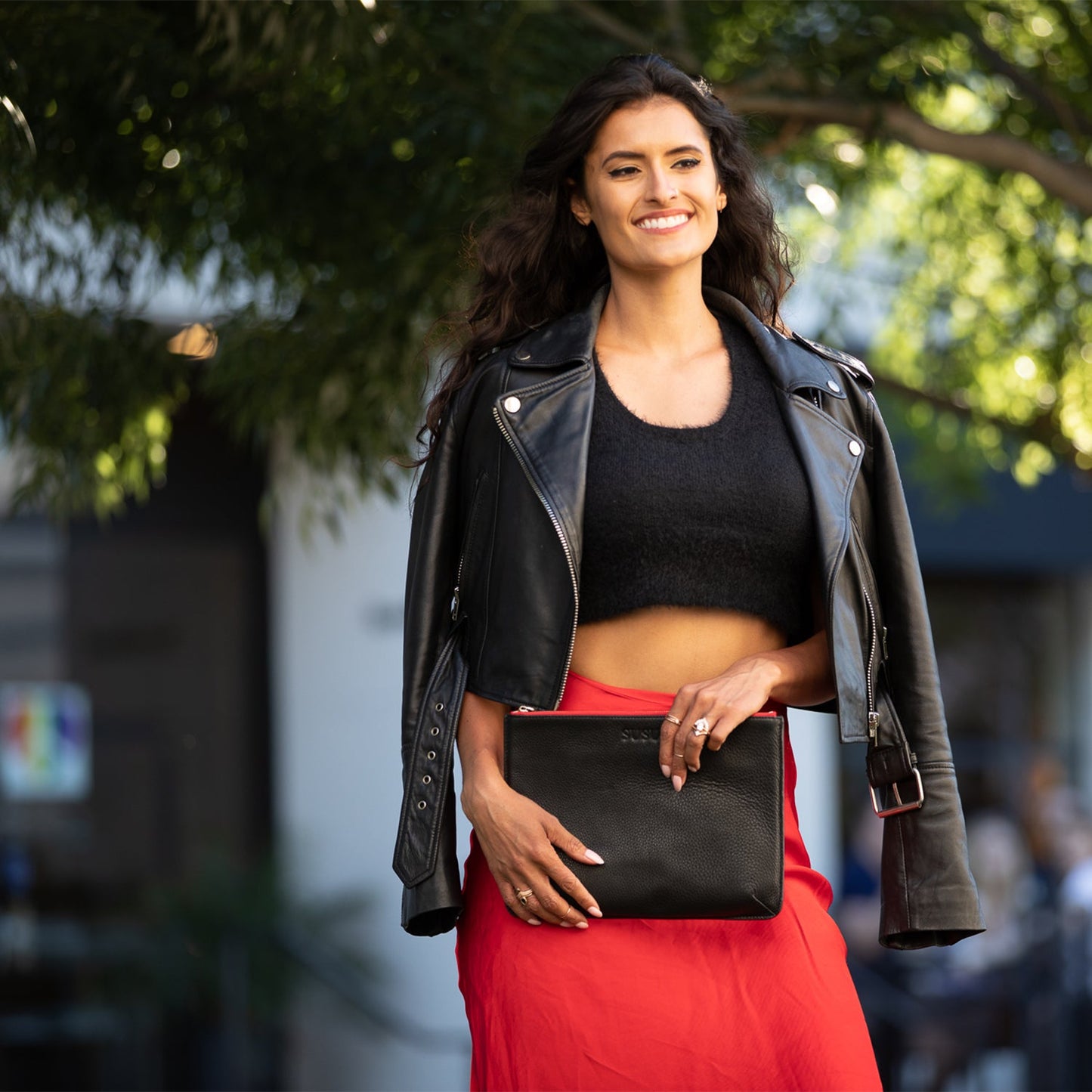 Woman holding a black clutch bag outdoors with blurred background