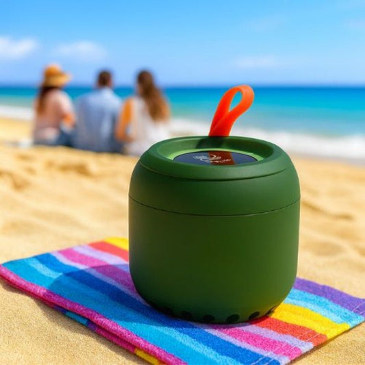 Green portable Bluetooth Speaker on a colorful towel with people in the background at the beach