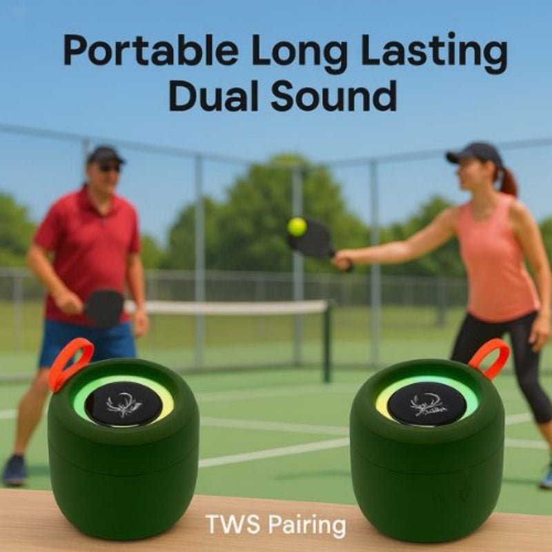 Two green portable speakers with orange handles on a table, with people playing pickleball in the background.