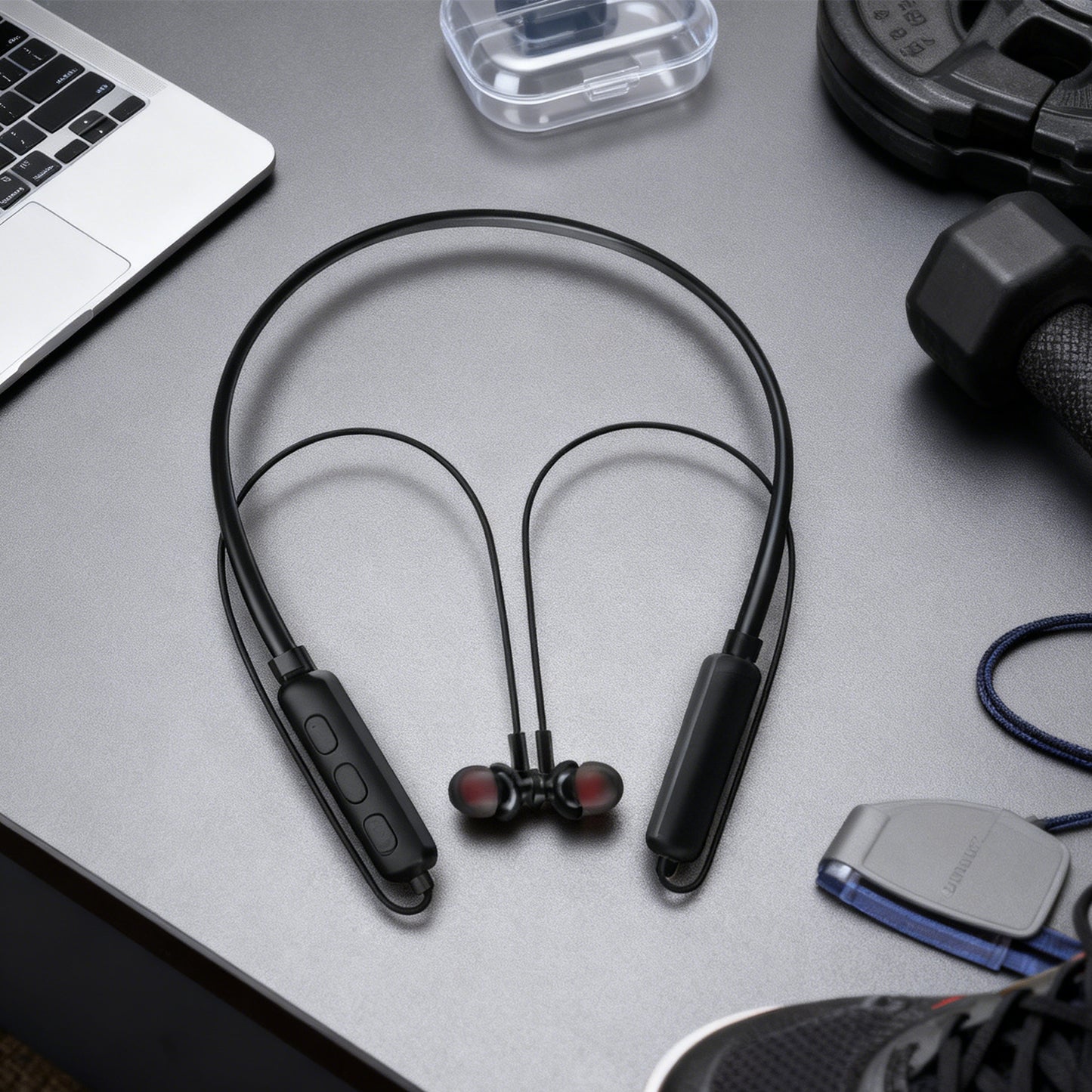 Black wireless earbuds on a gray surface with a laptop and other items.