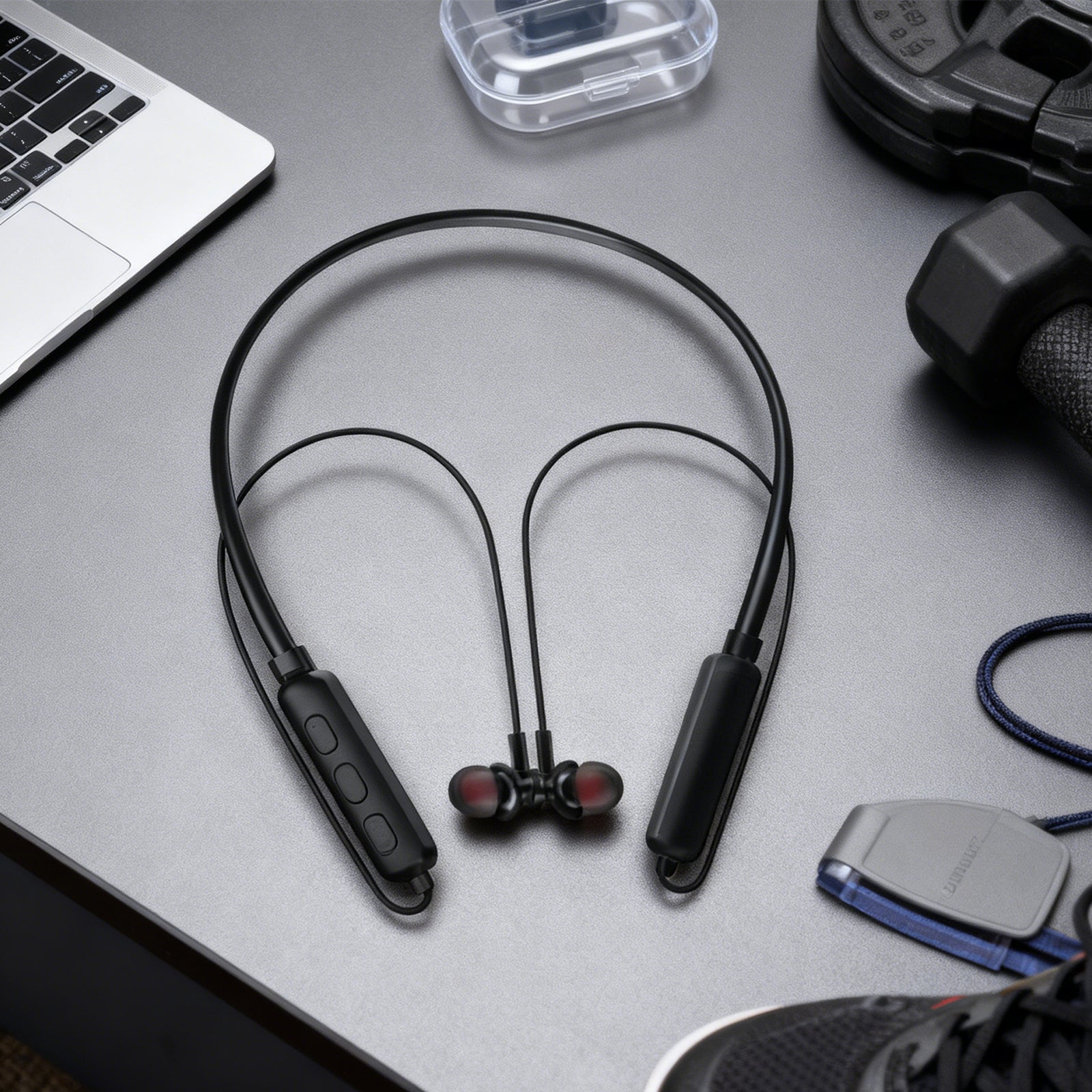 Black wireless earbuds on a gray surface with a laptop and other items.